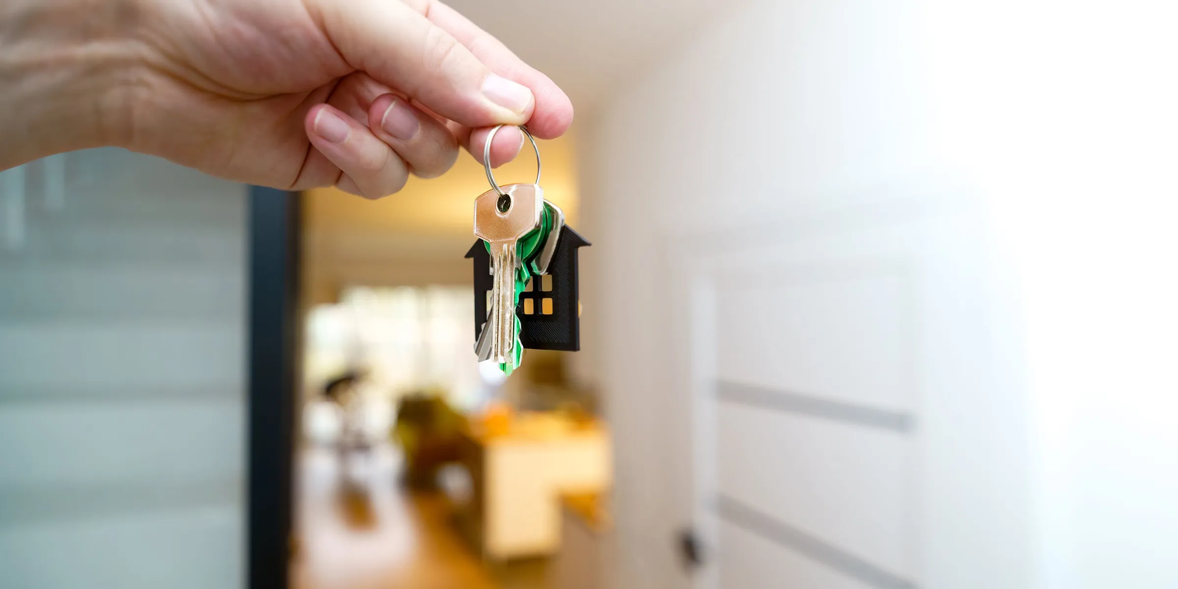 Eine Hand hält einen Schlüsselbund mit Haus-Anhänger in einer geöffneten Wohnungstür