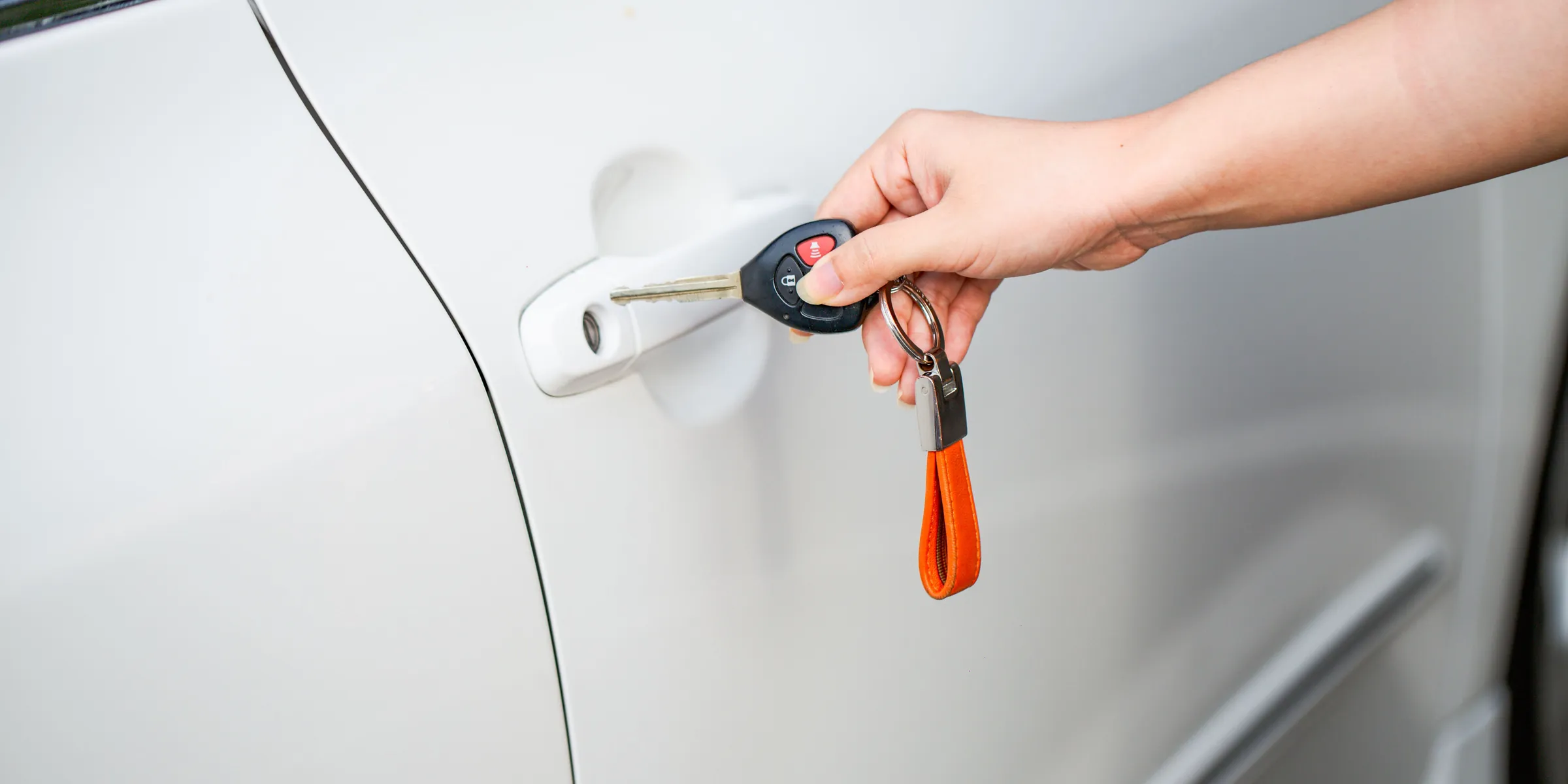 Hand mit Autoschlüssel und orangem Anhänger an der Tür eines weißen Autos