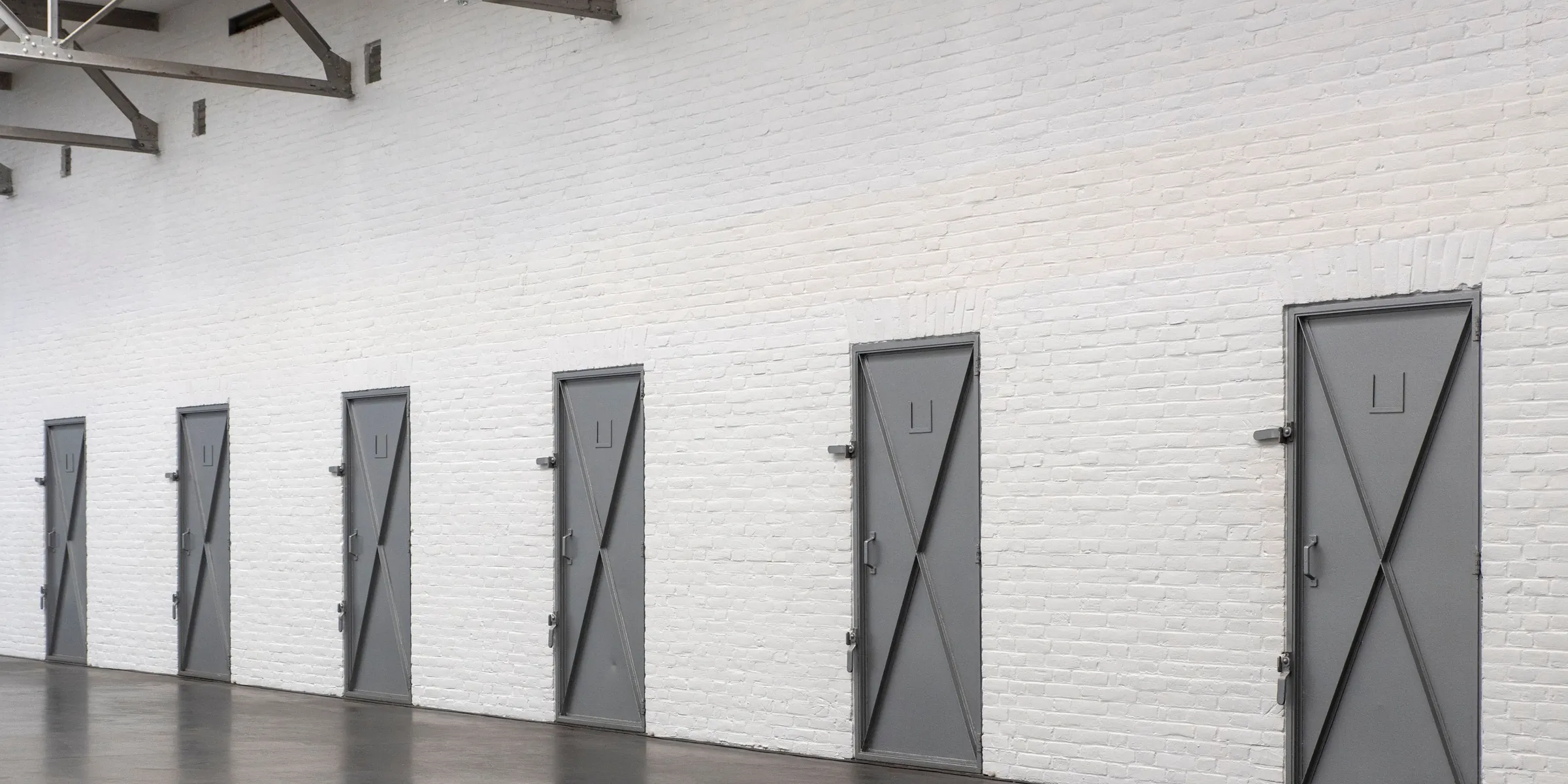 Lagerhalle mit weißer Backsteinwand und einer Reihe grauer Metalltüren zu einzelnen Lagerräumen