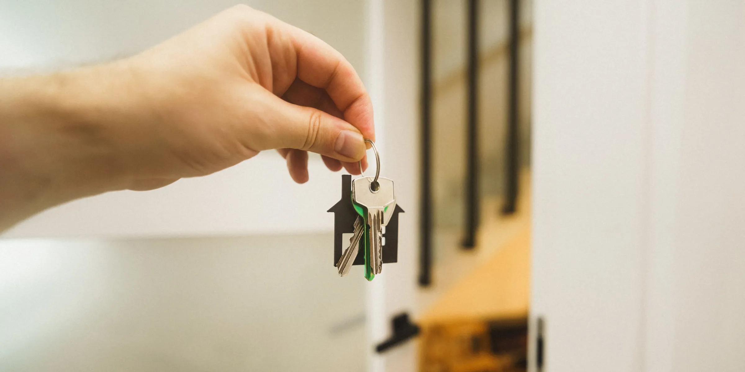 Eine Hand hält einen Wohnungsschlüssel mit Hausanhänger vor einer geöffneten Wohnungstür