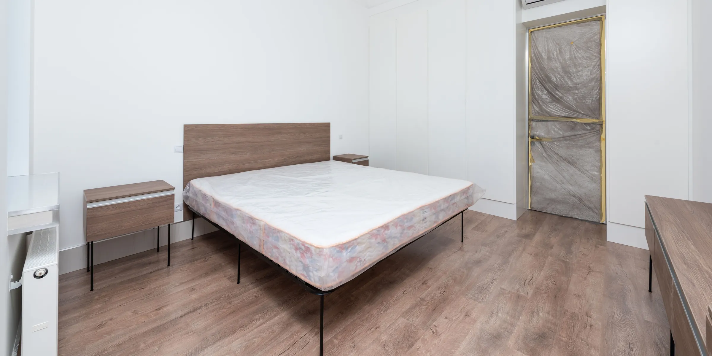 Unbezogene Matratze auf einem Bettgestell in einem leeren, hellen Schlafzimmer